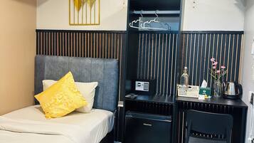 A hotel room with a bed, a desk, a chair, a small fridge, a heater, and a wall-mounted air conditioner.