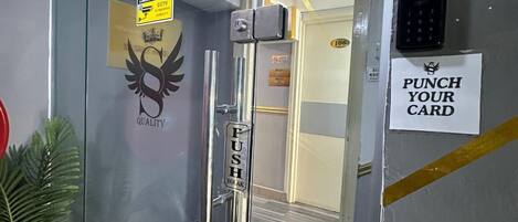 A reception area with a glass door, a welcome sign, a reception sign, a CCTV sign, a punch card sign, and a sign with a phone number.