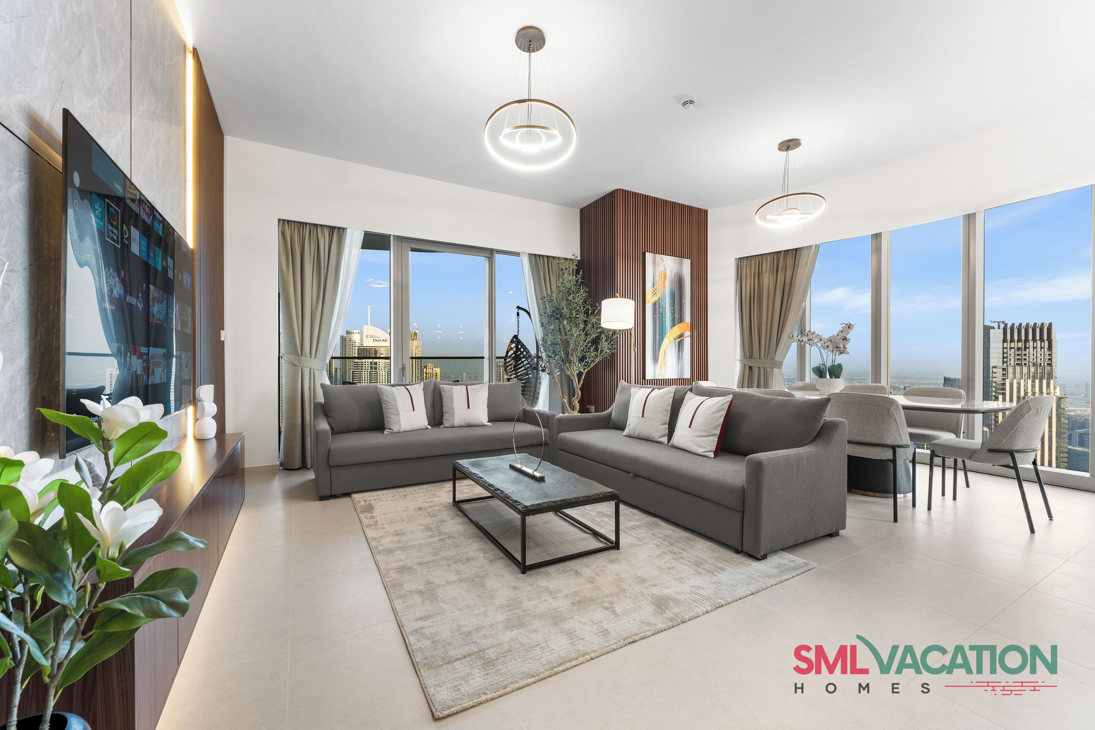 A modern living room with a sofa, coffee table, and dining area, large windows with a city view, and a plant.