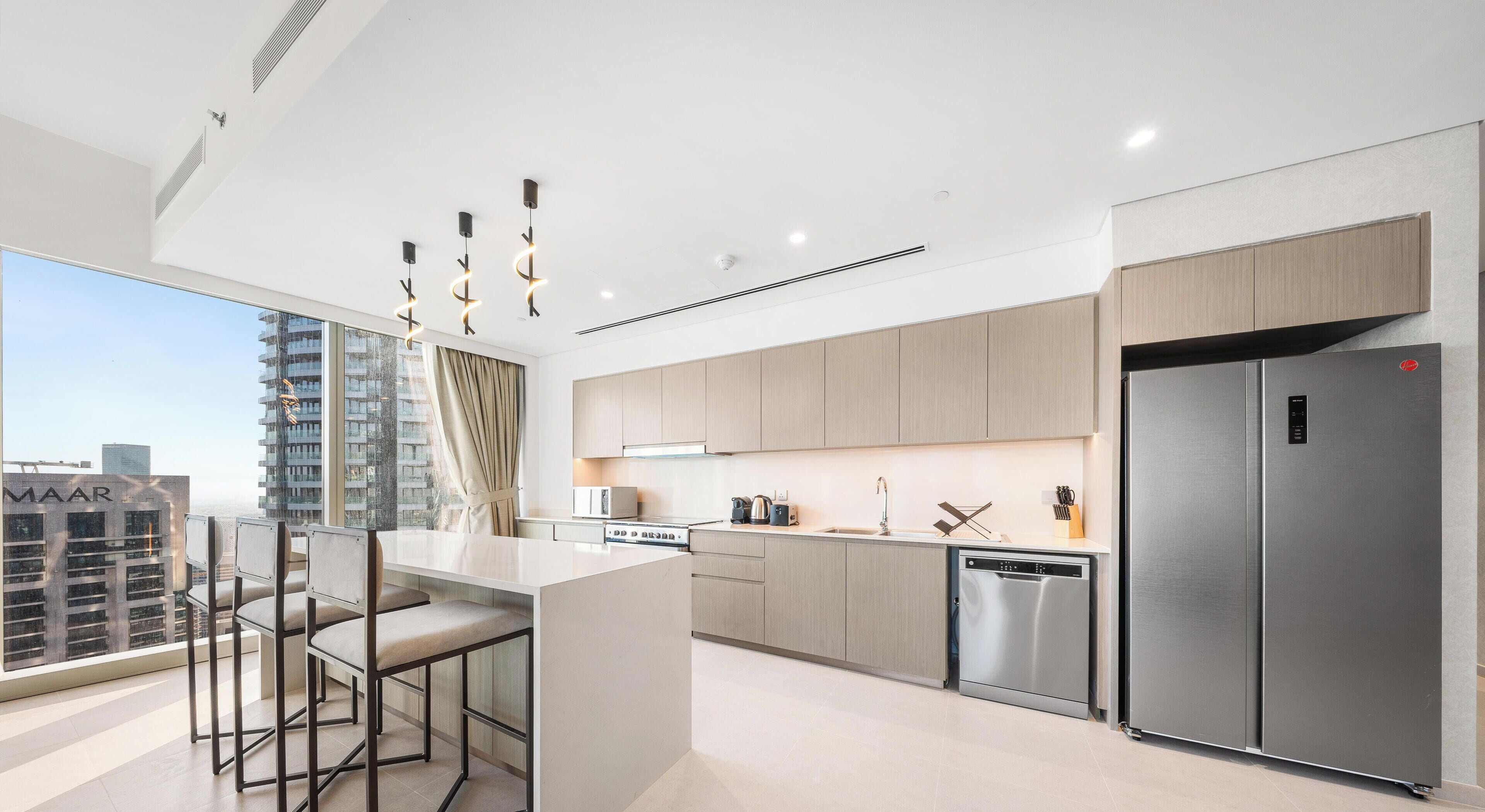 A modern kitchen with a stainless steel refrigerator, a built-in oven, and a large window overlooking a cityscape.