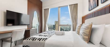 A modern hotel room with a large bed, a flat-screen TV, a desk, and a city view.