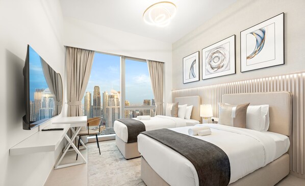 A modern hotel room with two beds, a desk, and a large window offering a city view. - SML Vacation Homes - Sky High Apartments with Burj Khalifa and Dubai Fountain Views @ Grande Signature, Downtown Dubai (Dubai)