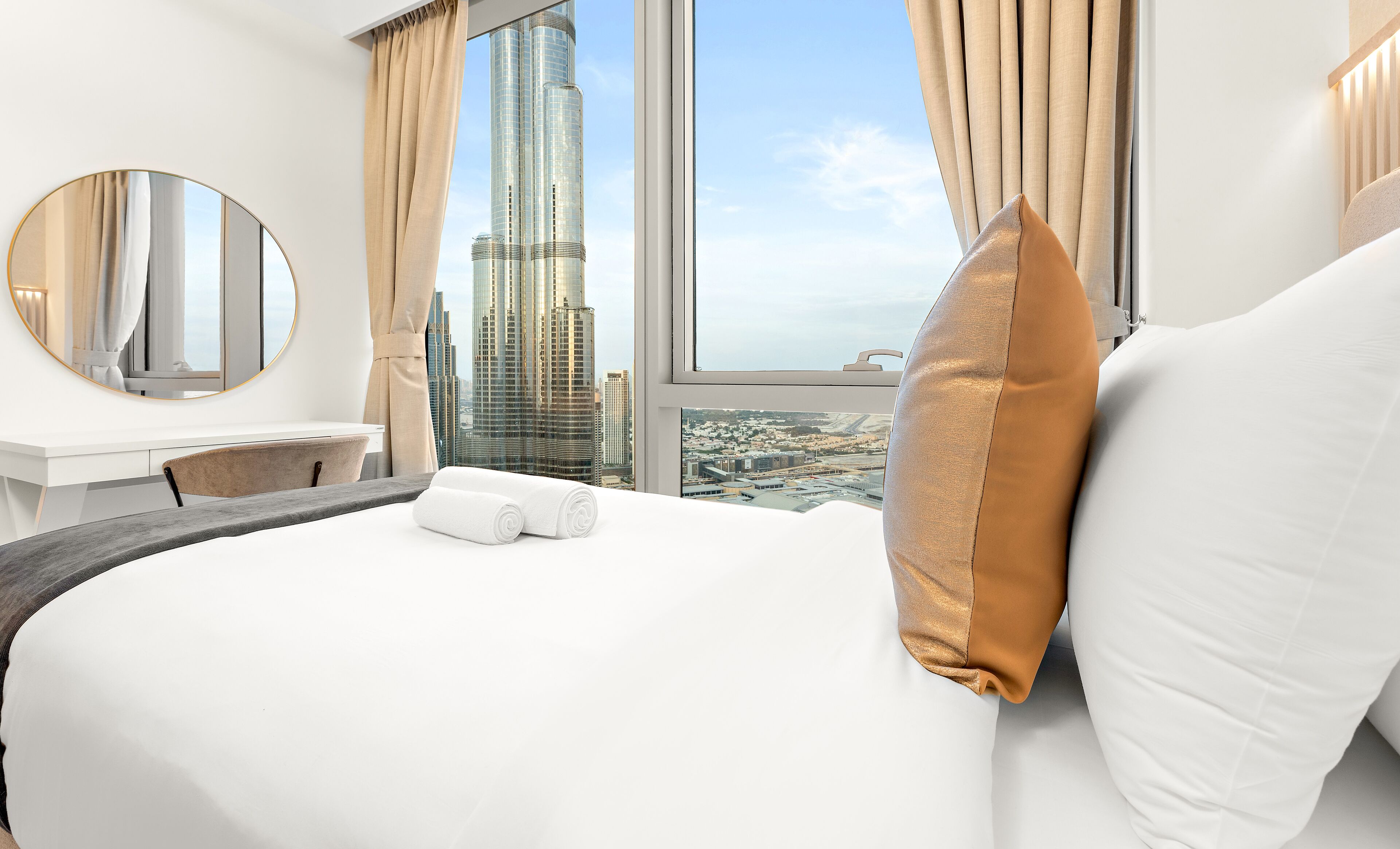 Une chambre d’hôtel avec un grand lit, un miroir rond, une vue sur un immeuble imposant et un panorama sur la ville.