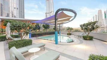 A rooftop pool area with lounge chairs, a pool, and a view of tall buildings.