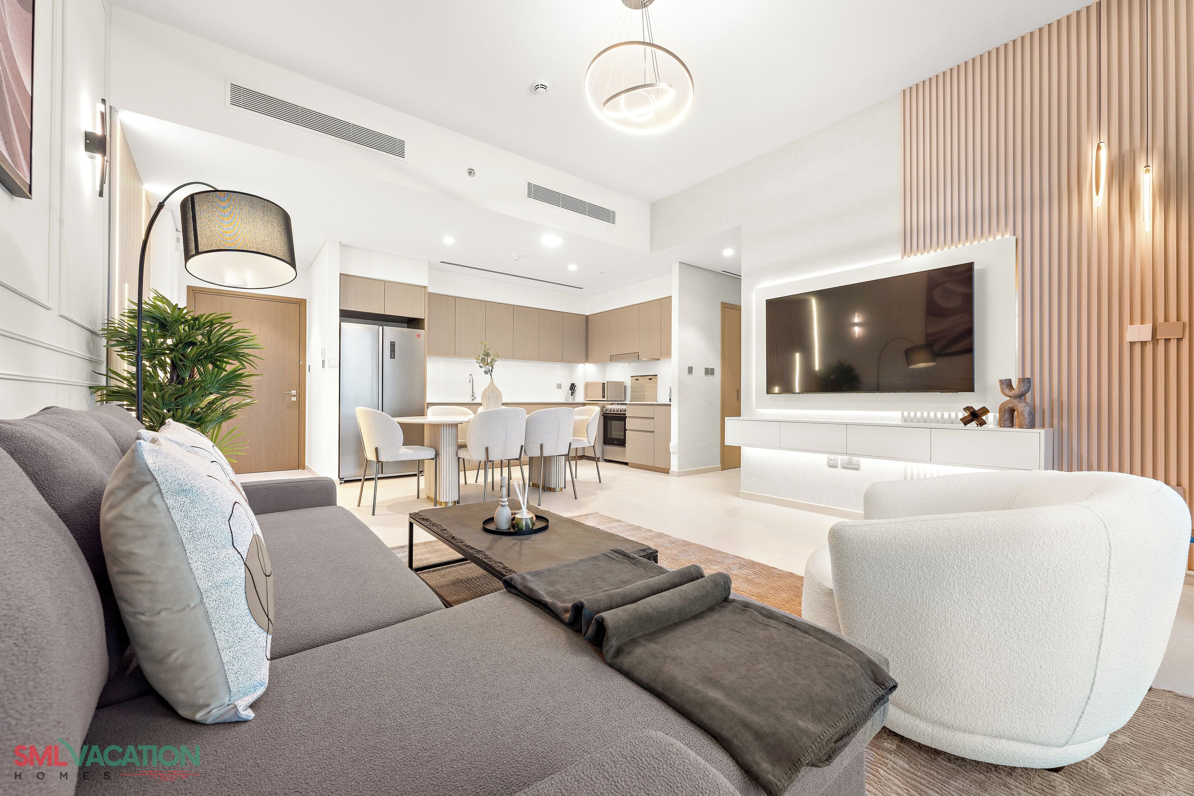 A modern living room with a grey sofa, a white armchair, and a flat-screen TV mounted on the wall.