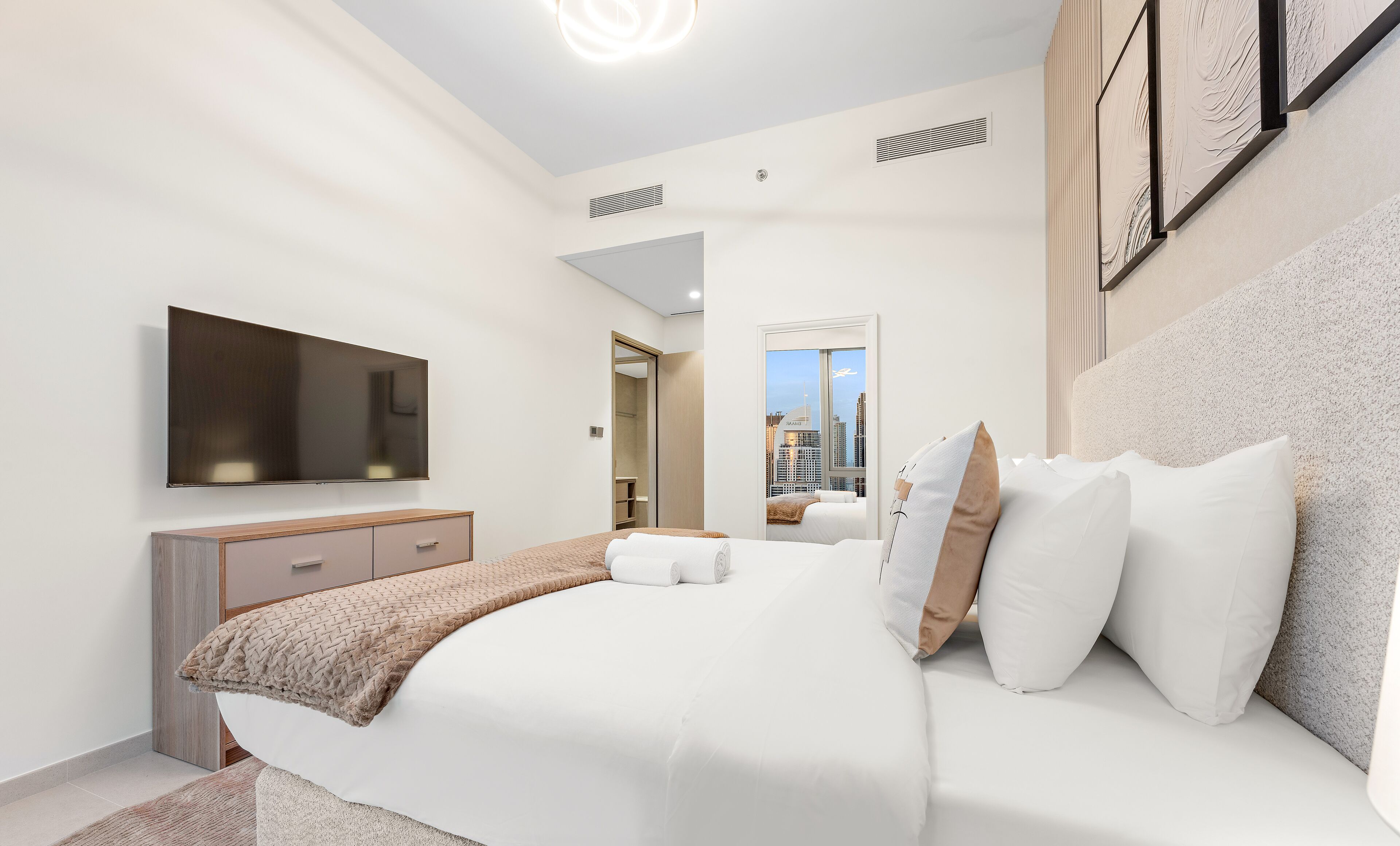 A modern hotel room with a large bed, a flat-screen TV, a wooden cabinet, and a city view.
