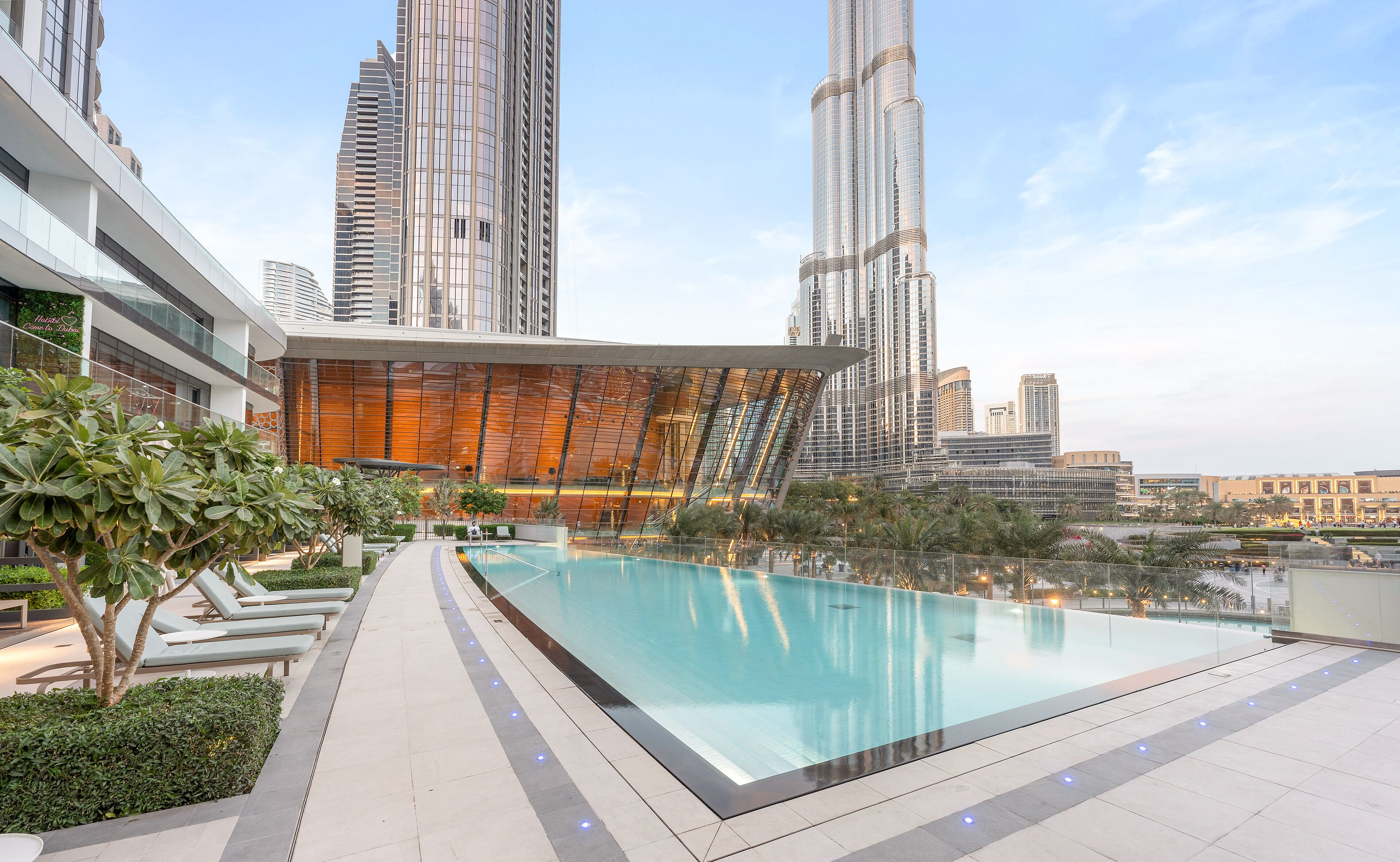 A rooftop pool with a glass barrier, surrounded by modern buildings and palm trees.