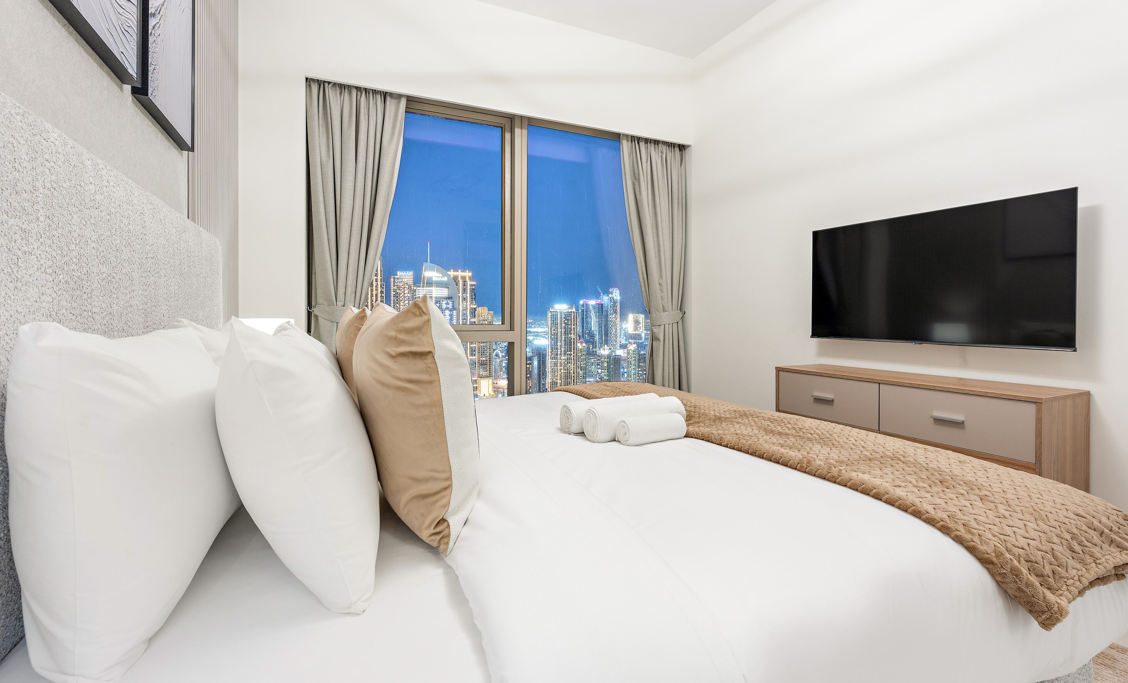 A hotel room with a bed, a TV, a city view, and a window with curtains.