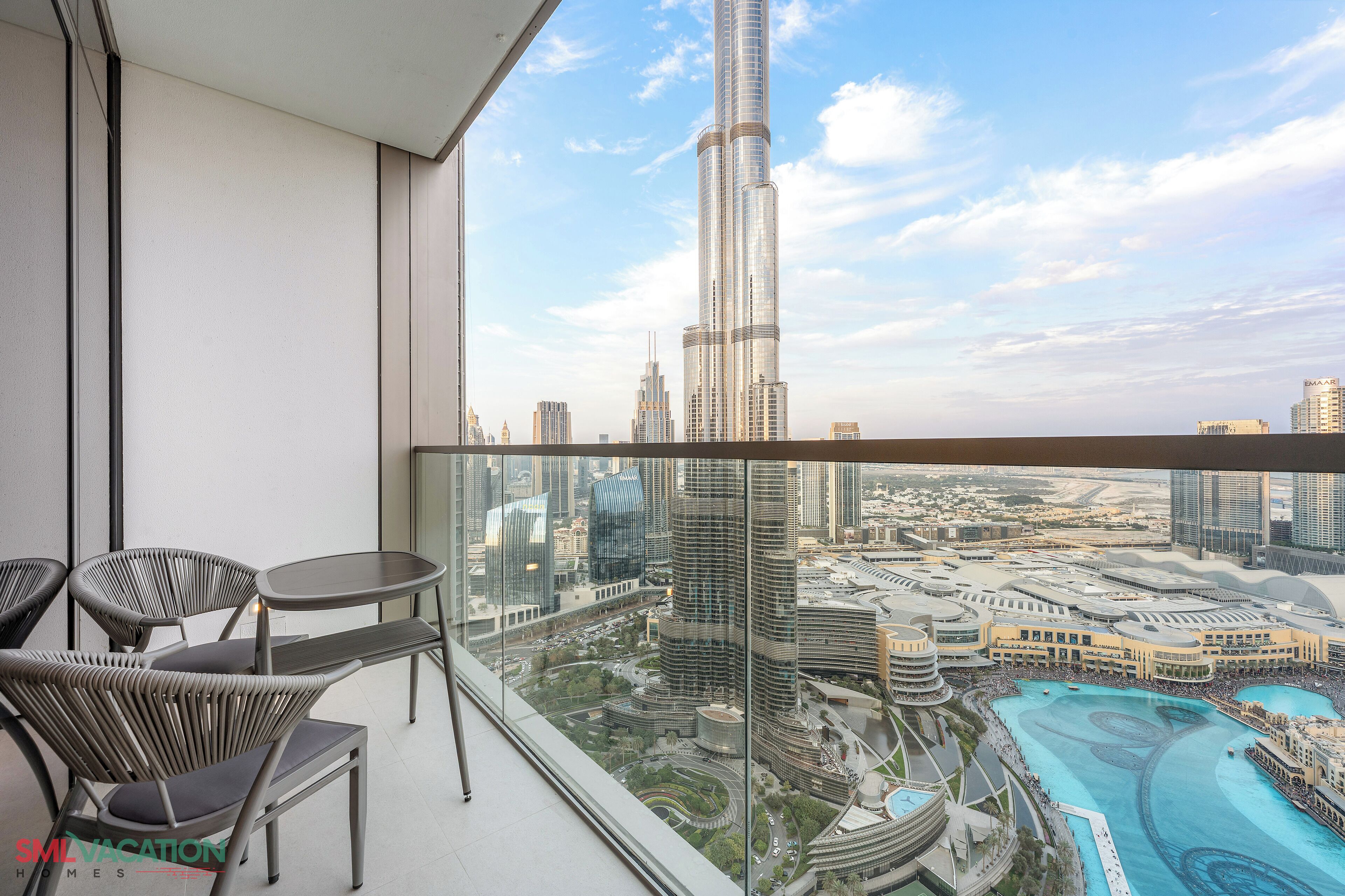 A balcony with a view of a cityscape, including a prominent skyscraper, modern buildings, and a water feature.