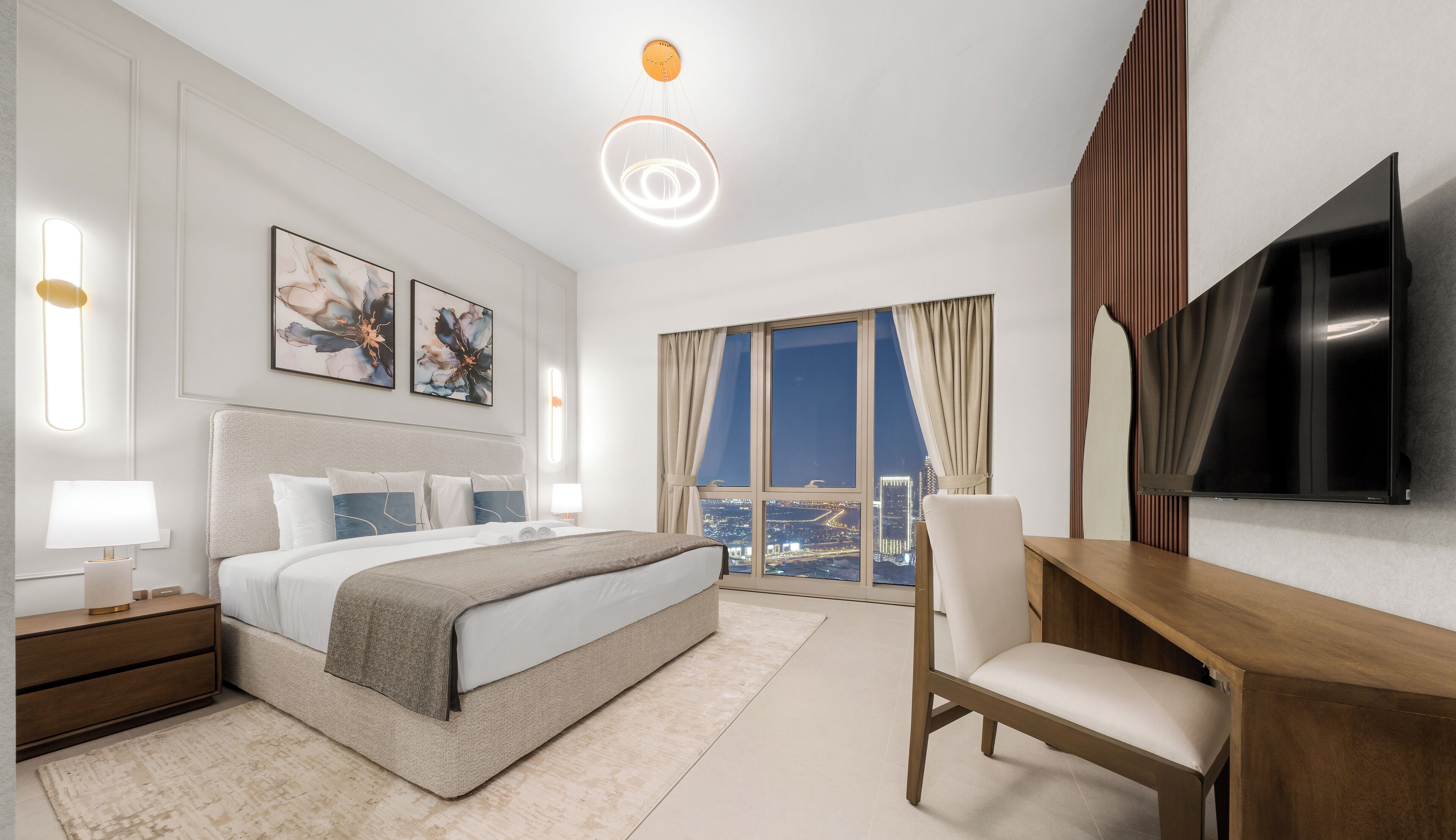 A modern hotel room with a bed, desk, TV, and large windows offering a city view.