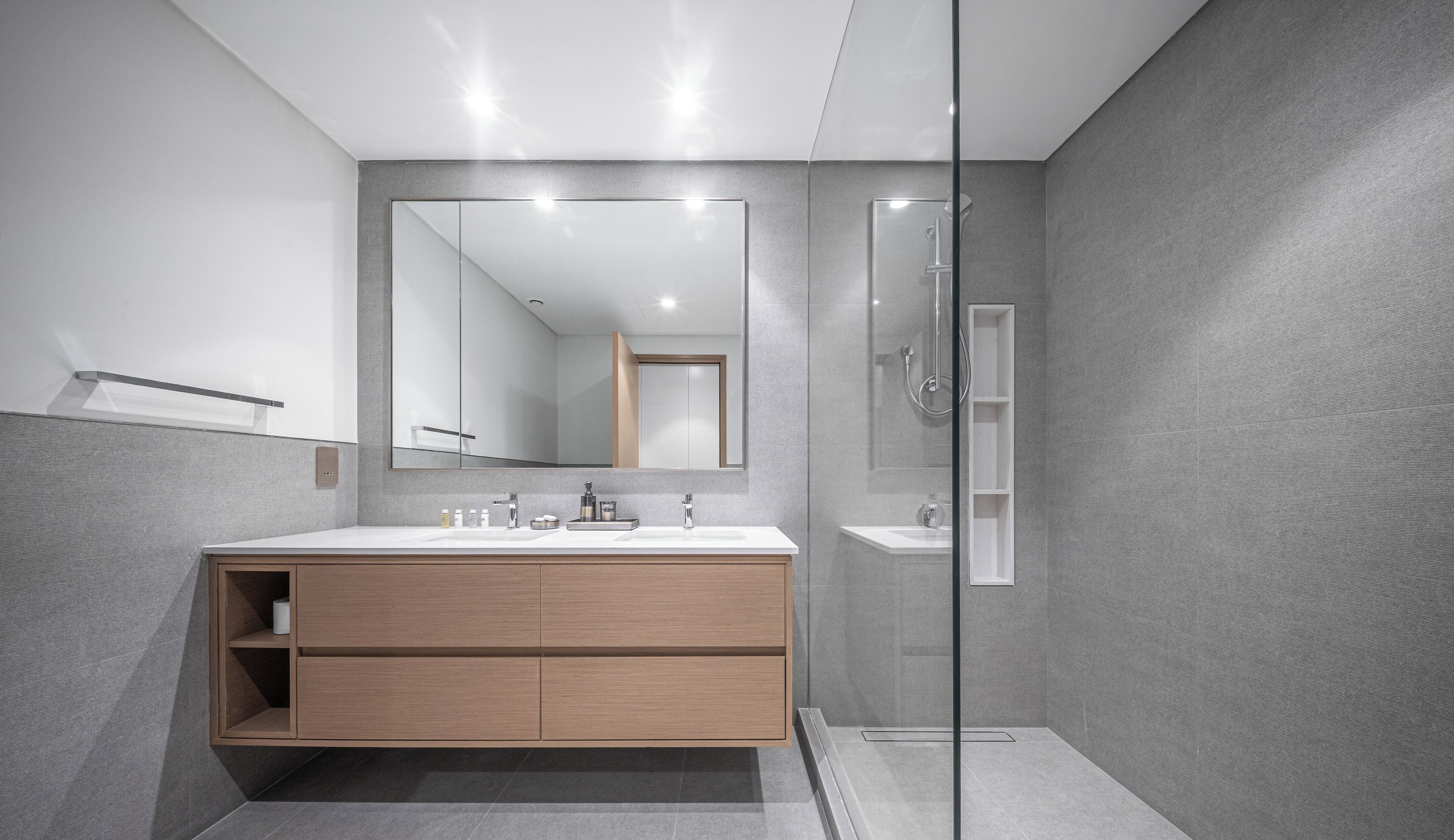 A modern bathroom with a large mirror, a glass shower enclosure, and a wooden vanity with a sink.