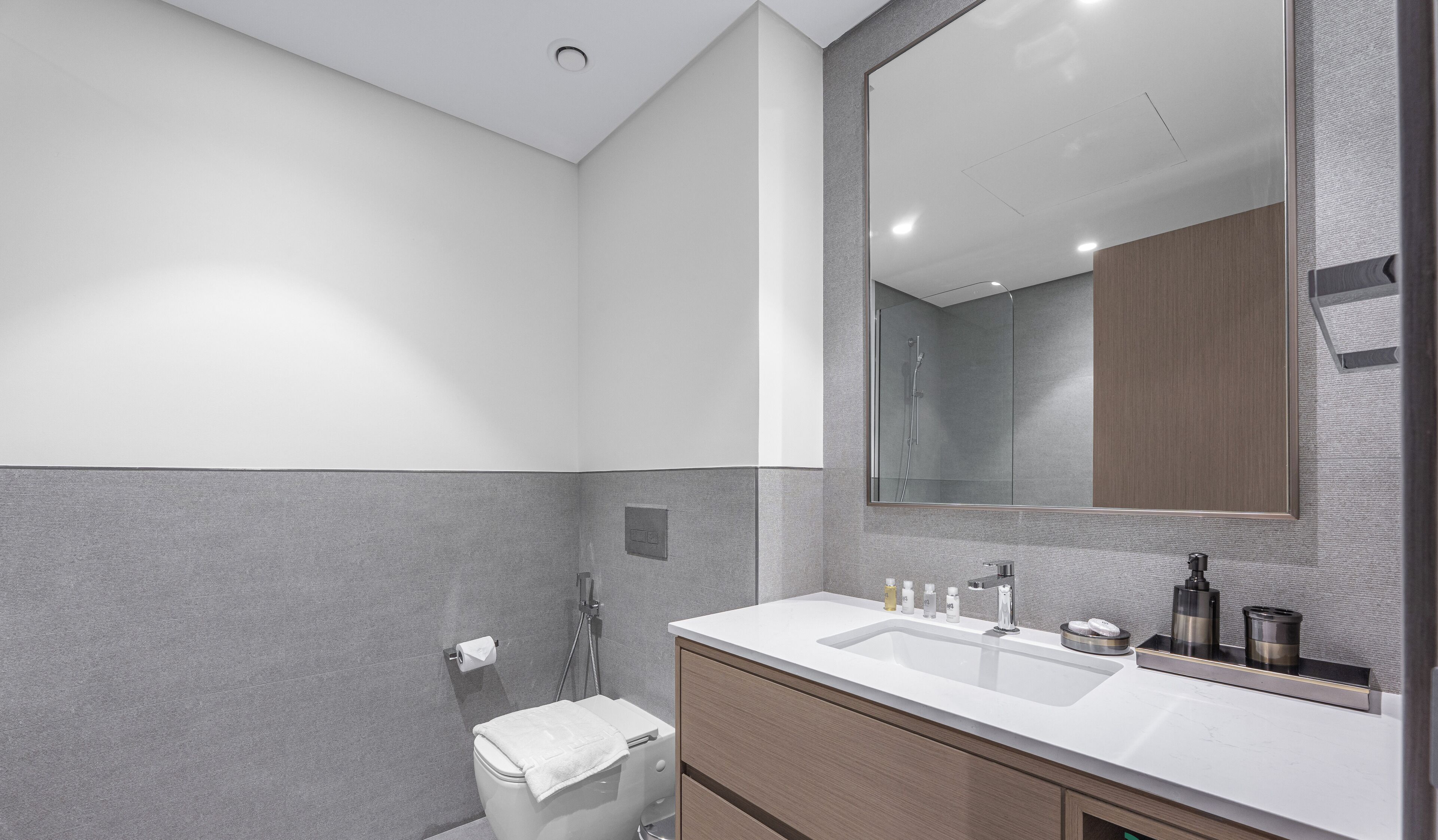 A modern bathroom with a large mirror, white sink, and a shower area.