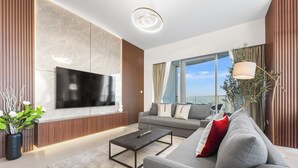 A modern living room with a flat-screen TV, a grey sofa, a coffee table, and a large window offering a city view. - SML Vacation Homes - Sky High Apartments with Burj Khalifa and Dubai Fountain Views @ Grande Signature, Downtown Dubai (Dubai)