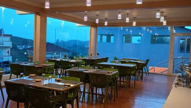 Un restaurante con varias mesas y sillas, amplias ventanas que ofrecen vistas del entorno y suelo de madera.