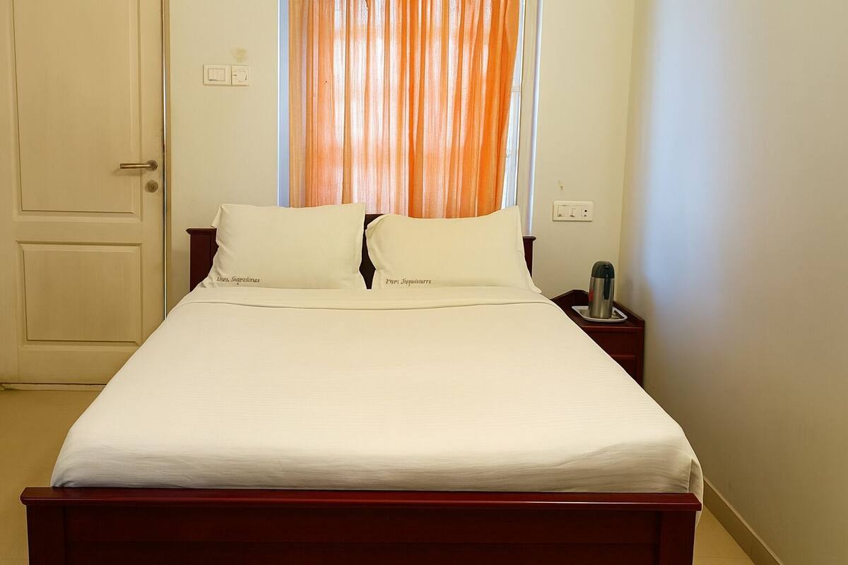 Una cama bien tendida con sábanas blancas, cabecera de madera y mesita de noche con tetera.