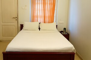A neatly made bed with white linens, a wooden headboard, and a nightstand with a kettle.