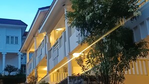 Un hotel de varios pisos con balcones, un muro de piedra de contención y un árbol en primer plano.