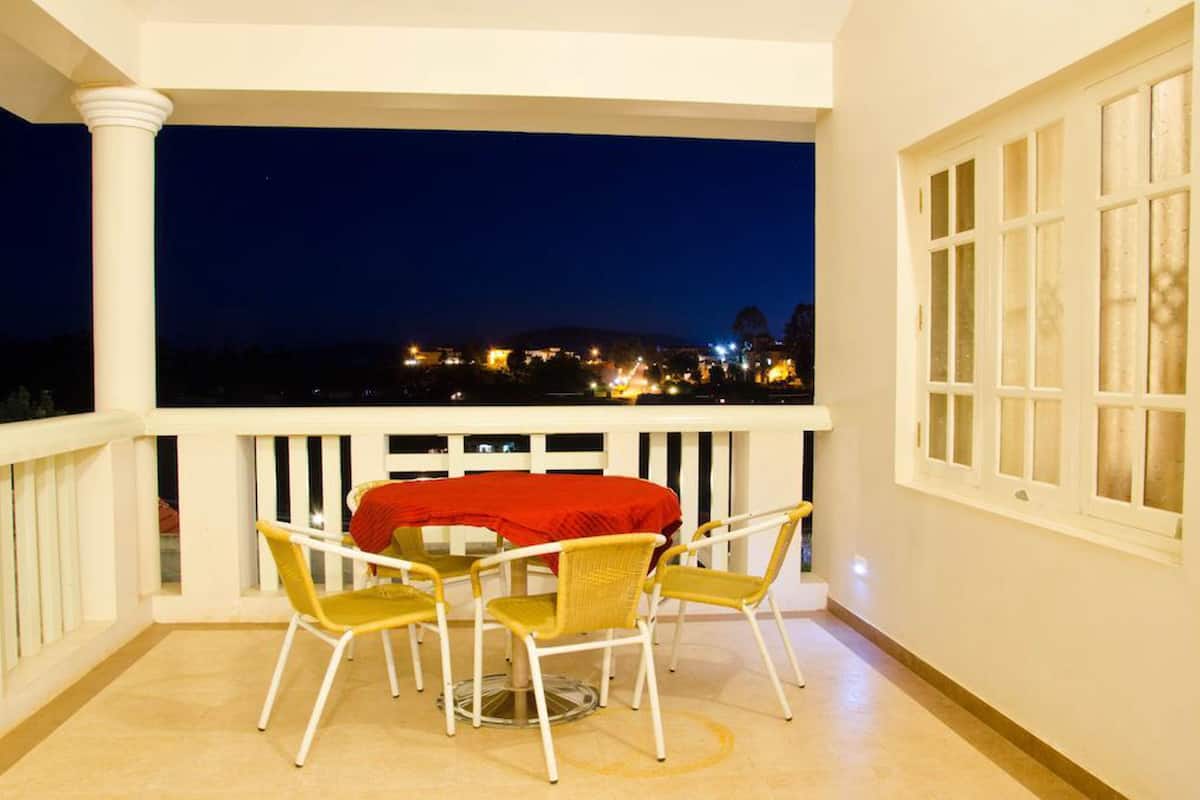 Un balcón con mesa y sillas, mantel rojo y vista a un paisaje urbano de noche.