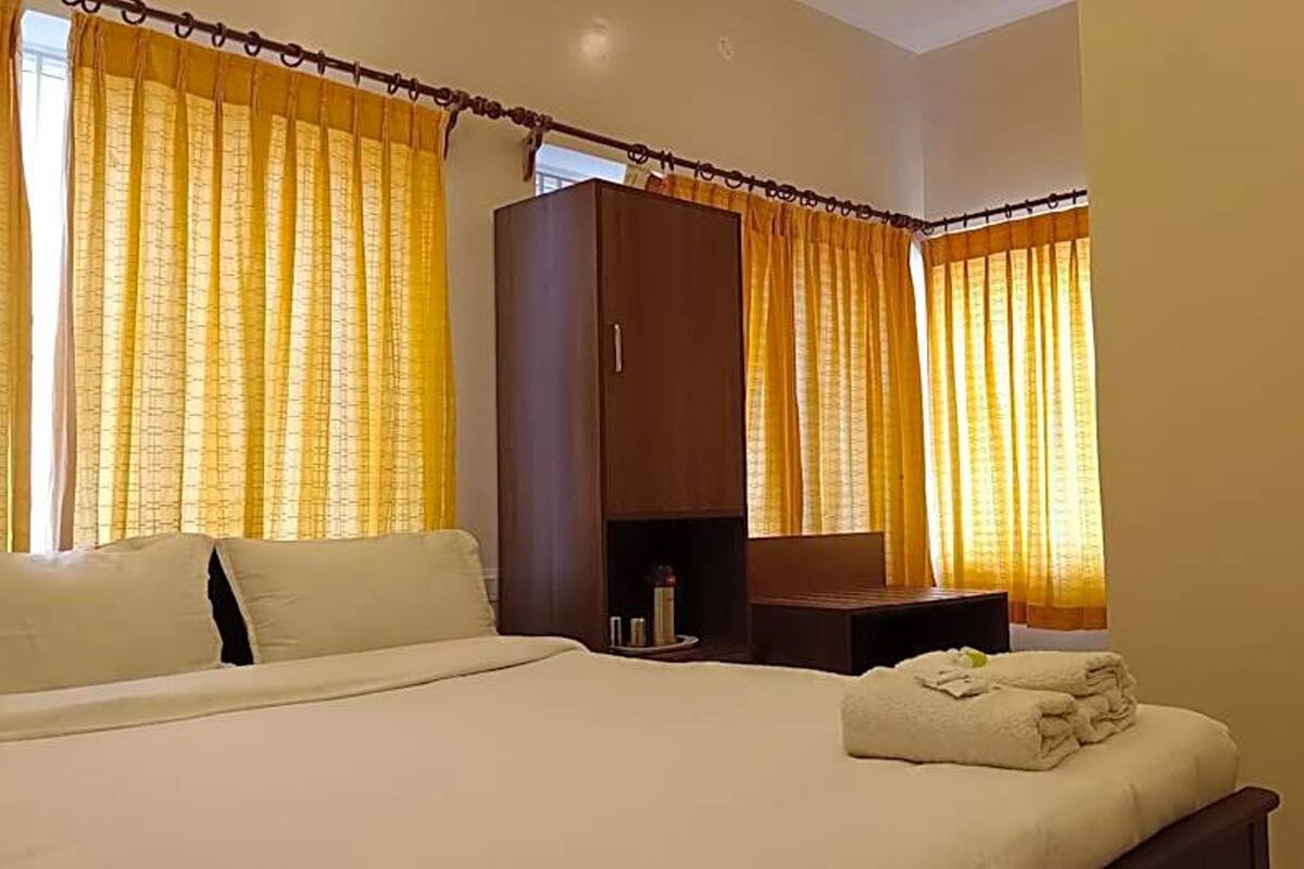 Una habitación de hotel con cama, armario, mesita de noche y cortinas.