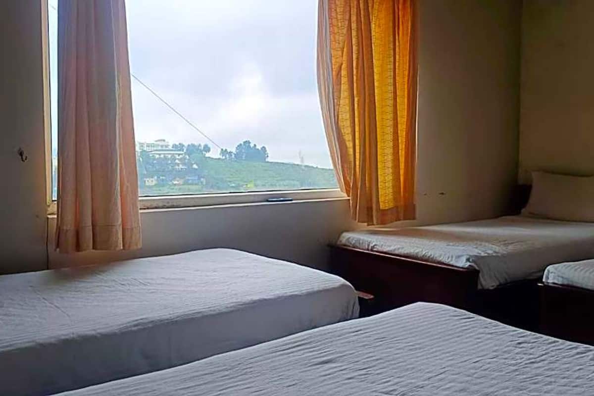 Una habitación con dos camas individuales, una ventana con cortinas y vistas a un paisaje verde.