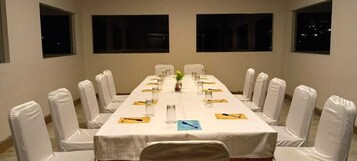 A conference room with a long table, white chairs, and a white tablecloth.
