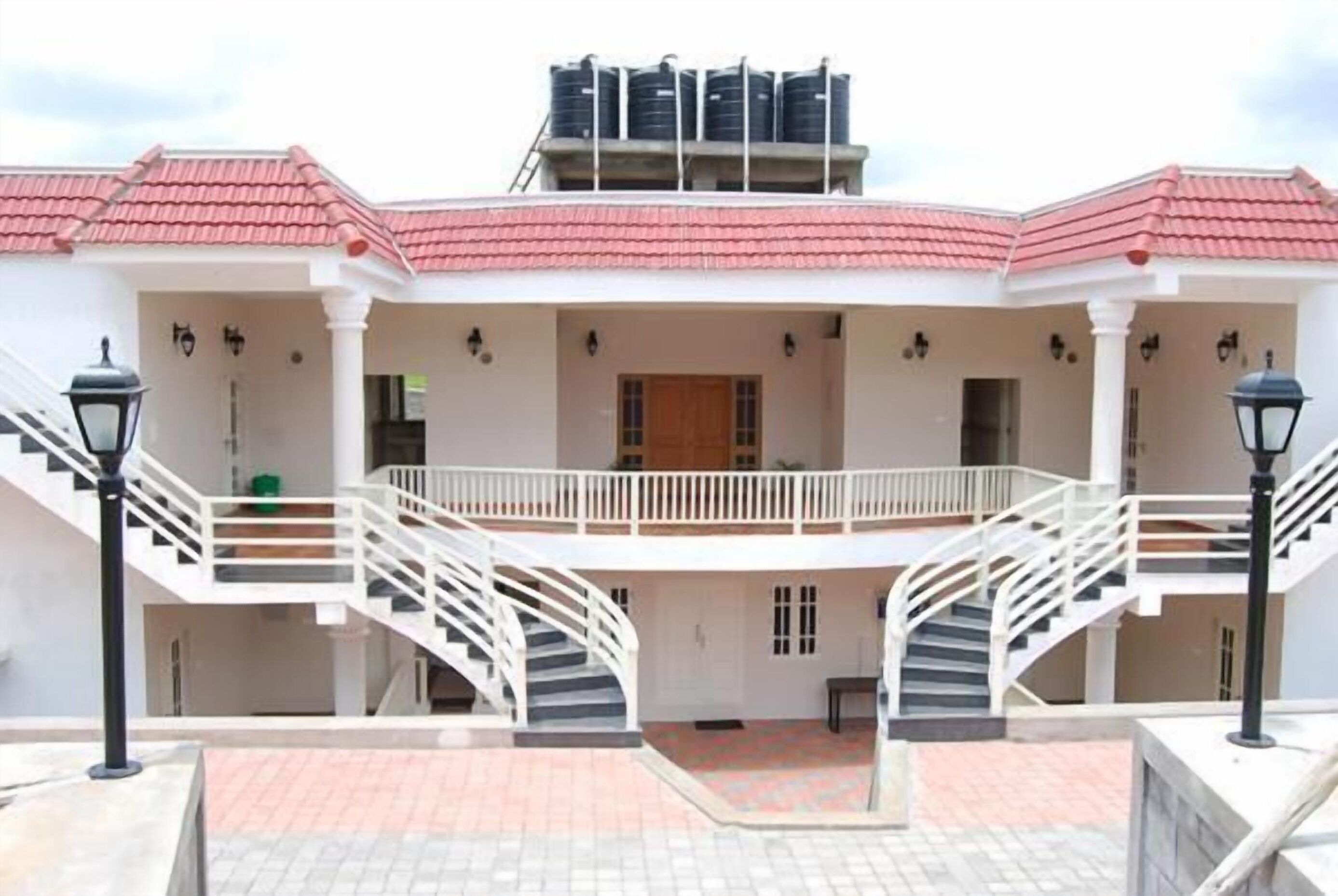 A two-story building with a red-tiled roof, white exterior walls, and a central courtyard with a staircase leading to the upper floor.