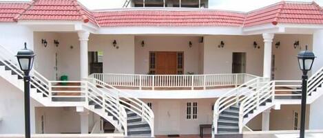 A two-story building with a red-tiled roof, white exterior walls, and a central courtyard with a staircase leading to the upper floor.