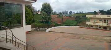 A terrace with a view of terraced fields, a building with a balcony, and a staircase leading to an upper level.