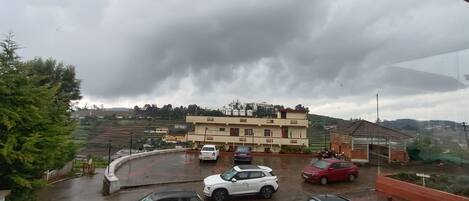 Un aparcamiento con varios coches, un edificio de varios pisos y un paisaje montañoso al fondo.