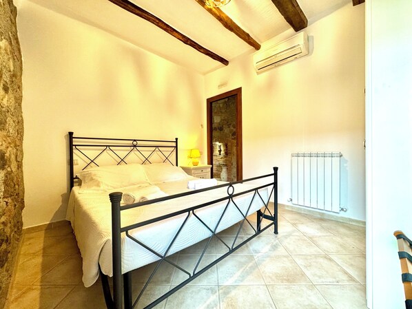 A bedroom with a bed, a nightstand, a lamp, a stone wall, and a radiator.
