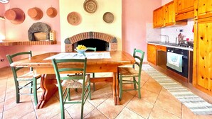 Un comedor con una mesa y sillas de madera, una chimenea de ladrillo y una cocina con armarios y electrodomésticos de madera.