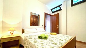 Un dormitorio con cama, mesita de noche, televisor montado en la pared y una puerta.