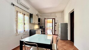 A compact kitchen with a dining table and chairs, a refrigerator, and a window with curtains. - "  Sea  Breeze  Home " (Lotzorai)