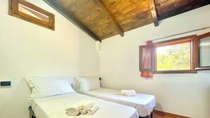 A room with two beds, a window with a curtain, and a wooden ceiling. - "  Sea  Breeze  Home " (Lotzorai)