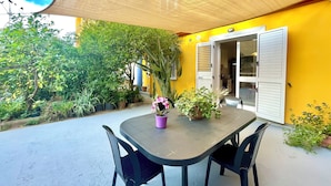 Eine Terrasse im Freien mit Tisch und Stühlen, umgeben von Kübelpflanzen und einer gelben Wand.