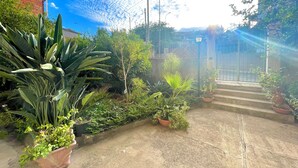 Ein Gartenweg führt zu einem verschlossenen Eingang mit Blumentöpfen und einem strahlend blauen Himmel.