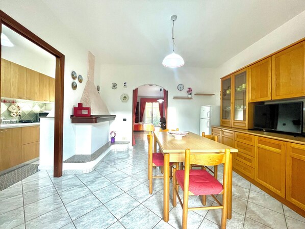 A spacious kitchen with wooden cabinets, a dining table with chairs, a built-in oven, and a television.