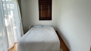 Une chambre à coucher avec un lit, une fenêtre avec des stores, un luminaire au plafond et une vue sur l’extérieur.