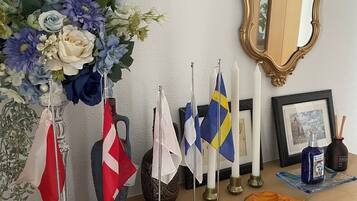 En byrå i trä med en spegel, flaggor, ljus och en vas med blommor.