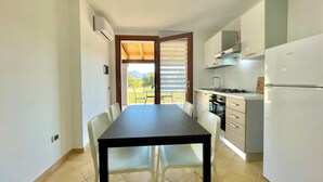 A compact kitchen with a dining table and chairs, a built-in oven, and a refrigerator. - " Cronta Apartments with patio " (Bari Sardo)