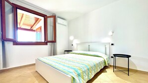 A bedroom with a bed, a window, and a wall-mounted air conditioner. - " Cronta Apartments with patio " (Bari Sardo)