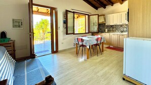 Ein Zimmer mit Esstisch, Stühlen, einer Küchenzeile und einem Balkon mit Blick auf Grünflächen.
