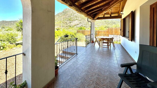 Eine überdachte Terrasse mit Tisch und Stühlen, einer Holzbalkendecke und Blick auf eine gebirgige Landschaft.