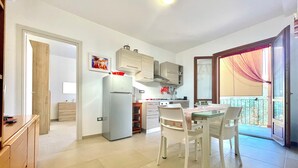 A modern kitchen with a refrigerator, stove, and dining area with chairs and a table. - " Beach House with Terrace " (Bari Sardo)