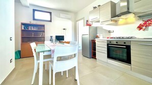 A modern kitchen with a dining area, including a table with chairs, a bookshelf, and a built-in oven. - " Beach House with Terrace " (Bari Sardo)