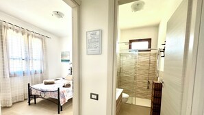 Hotellihuone, jossa on sänky, kylpyhuone lasiseinällä varustetulla suihkulla ja ikkunasta avautuva merinäköala.