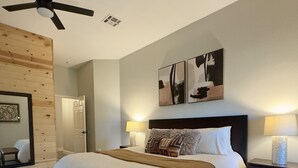 A modern bedroom with a bed, bench, ceiling fan, artwork, and a cowhide rug. - Spacious Family Gem, Close to Lake, Hot Tub (Lago Vista)