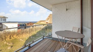 A balcony with a view of the sea, a white brick wall, and a table with chairs. - Strandperle - "Strandperle on Sylt: Your dream vacation with sea views and comfort!" (Wenningstedt-Braderup (Sylt))