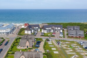 A coastal residential area with houses, a parking lot, and a beach in the background. - Strandperle - "Strandperle on Sylt: Your dream vacation with sea views and comfort!" (Wenningstedt-Braderup (Sylt))