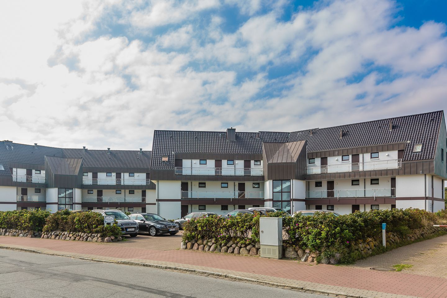 Un immeuble d’appartements moderne doté de nombreux balcons, d’un espace de stationnement et d’un jardin bien entretenu.
